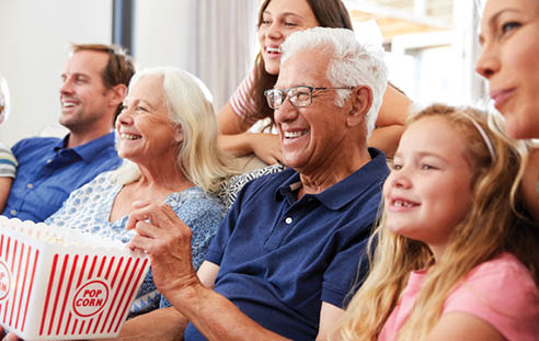 A group of people, including a man and a woman, are sitting on a couch and watching TV. They are holding a bag of popcorn. AI generated content